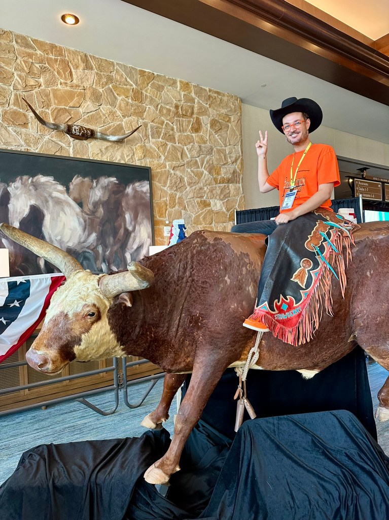 Kevie The Dreamer posing on a Texas longhorn display during Podcast Movement Dallas 2025.