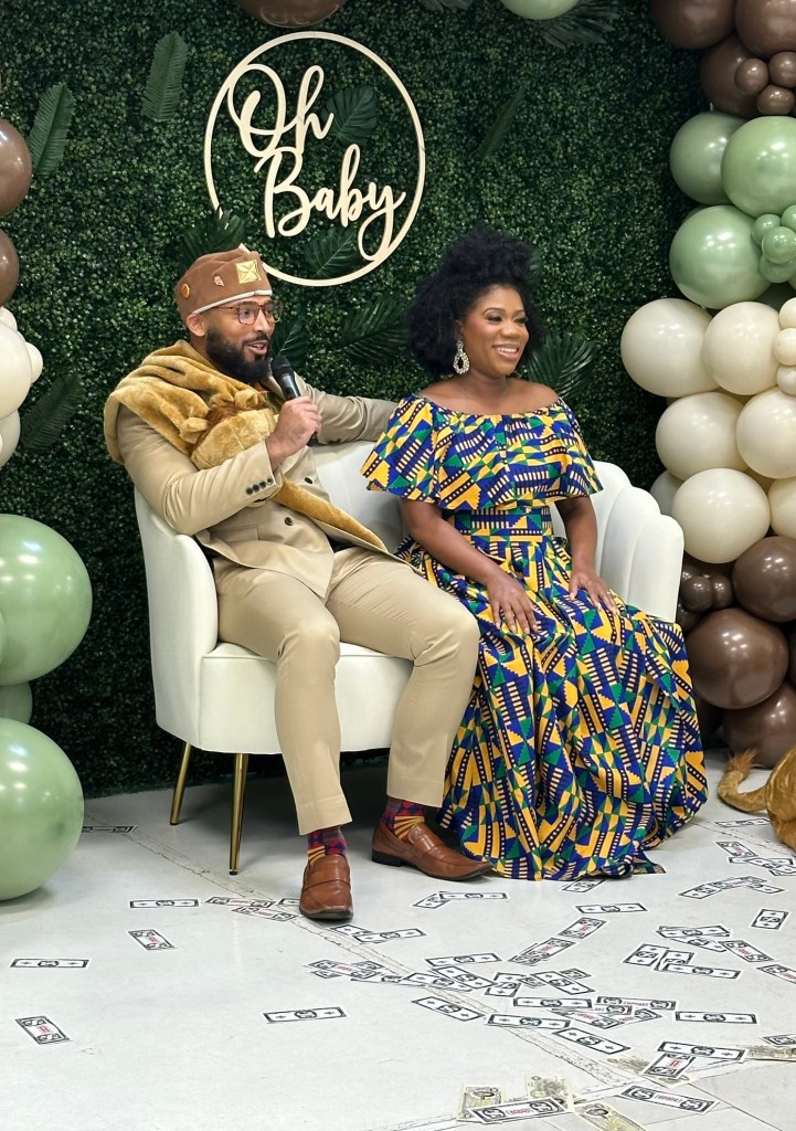 Parents-to-be seated on a decorative couch during Prince Elijah's Coming to America themed baby shower.